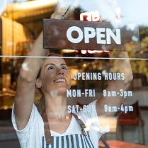 Photo representing Small Business, woman with "open" sign on store front
